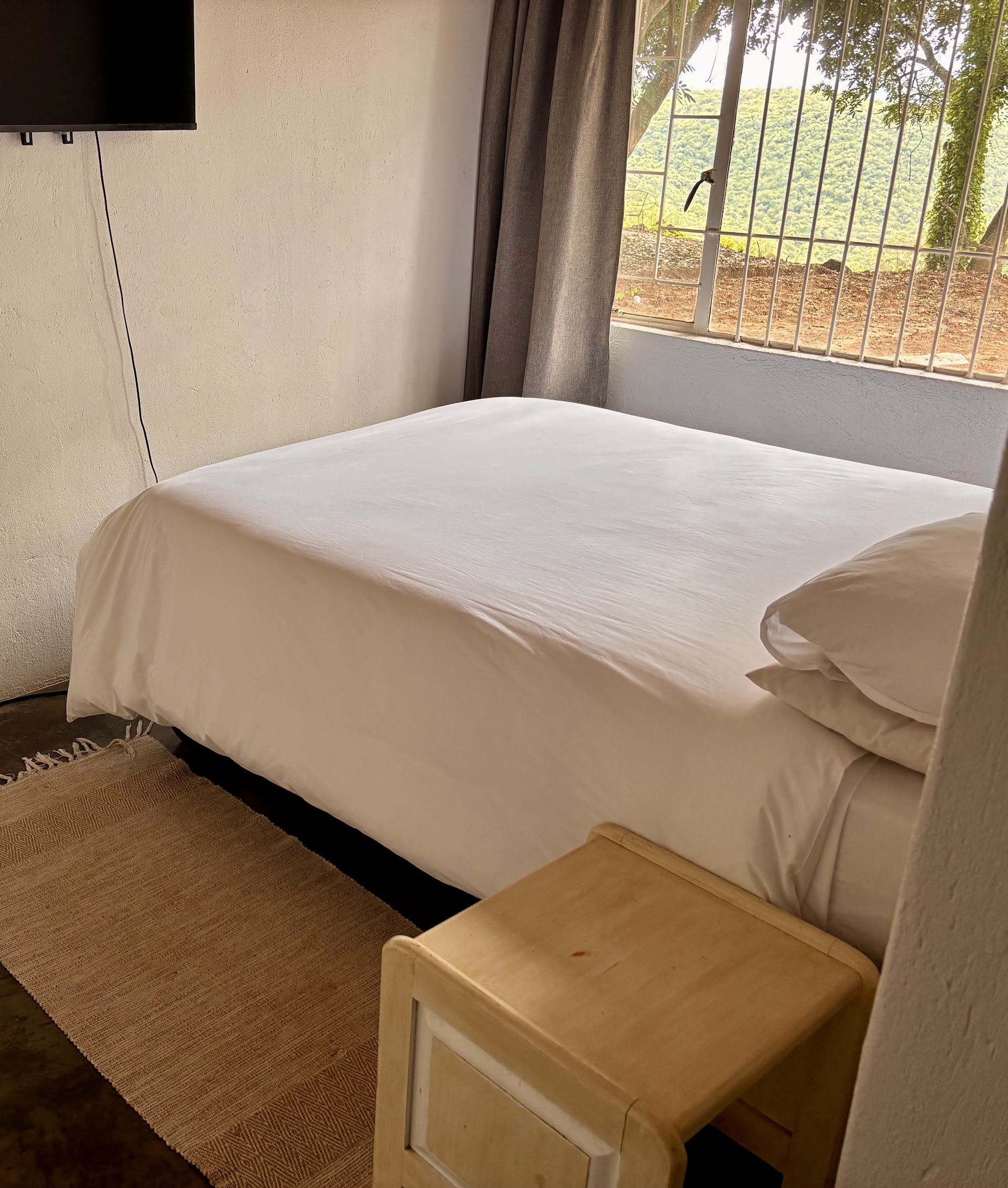 A lodge room at Kanaan Guest Farm — crisp white linen, simple side table, window onto the bushveld.
