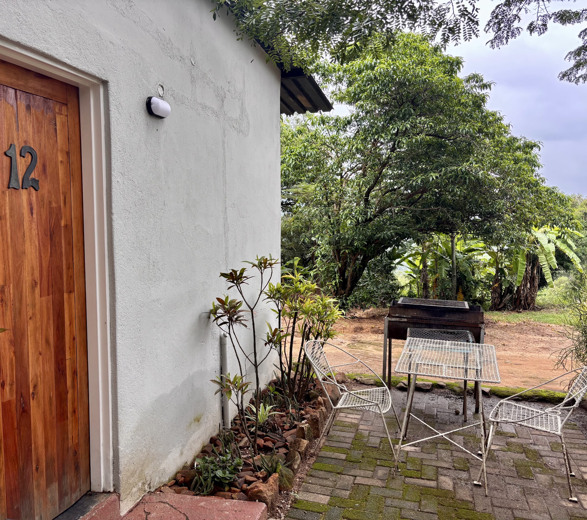 The front of a lodge unit at Kanaan — paved patio, a built-in braai under shade, and the bushveld just beyond.