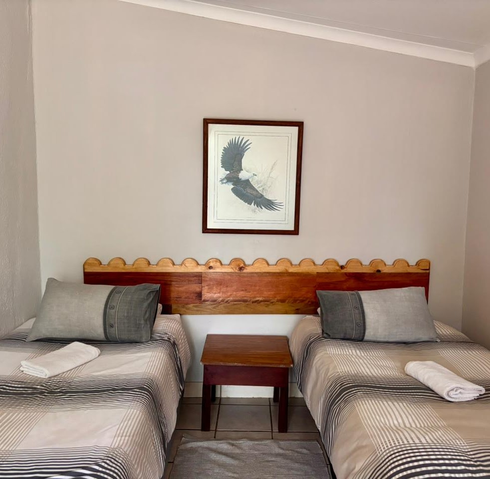 A basic twin room at Kanaan — two single beds with a scalloped wooden headboard, neutral linen, simple bedside table.