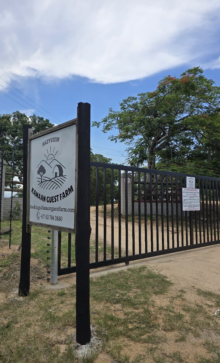 The Kanaan Guest Farm signboard at the front gate — black ironwork, the Hazyview lettering, a flame tree in flower behind it.