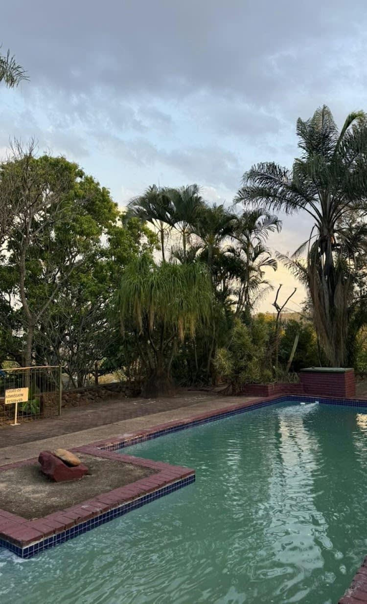 The pool at Kanaan at sunset — brick-paved edge, palms in silhouette, a soft pink and blue sky over the Lowveld beyond.