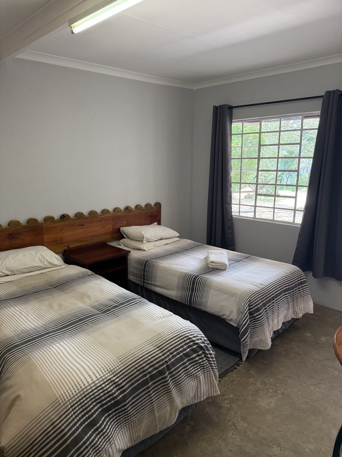 A twin room at Kanaan — two single beds with scalloped wooden headboards, neutral linen, a big window looking onto the trees.